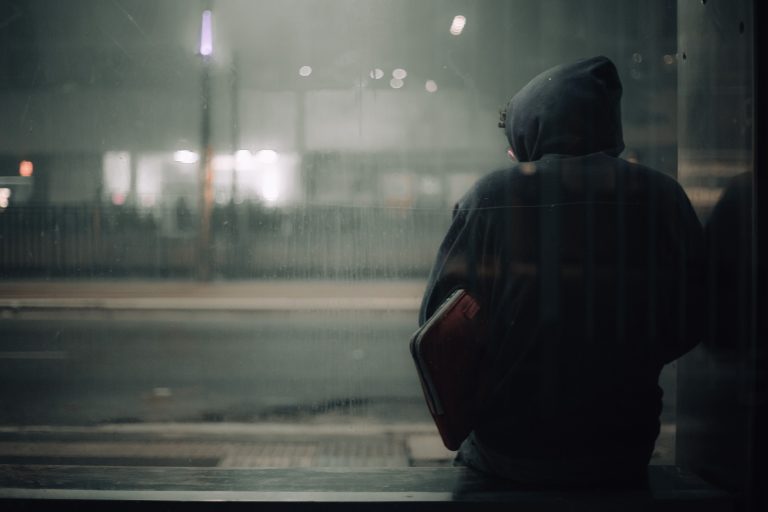 A person sits alone at night in an urban setting, reflecting the isolation that can drive people to seek connection.
