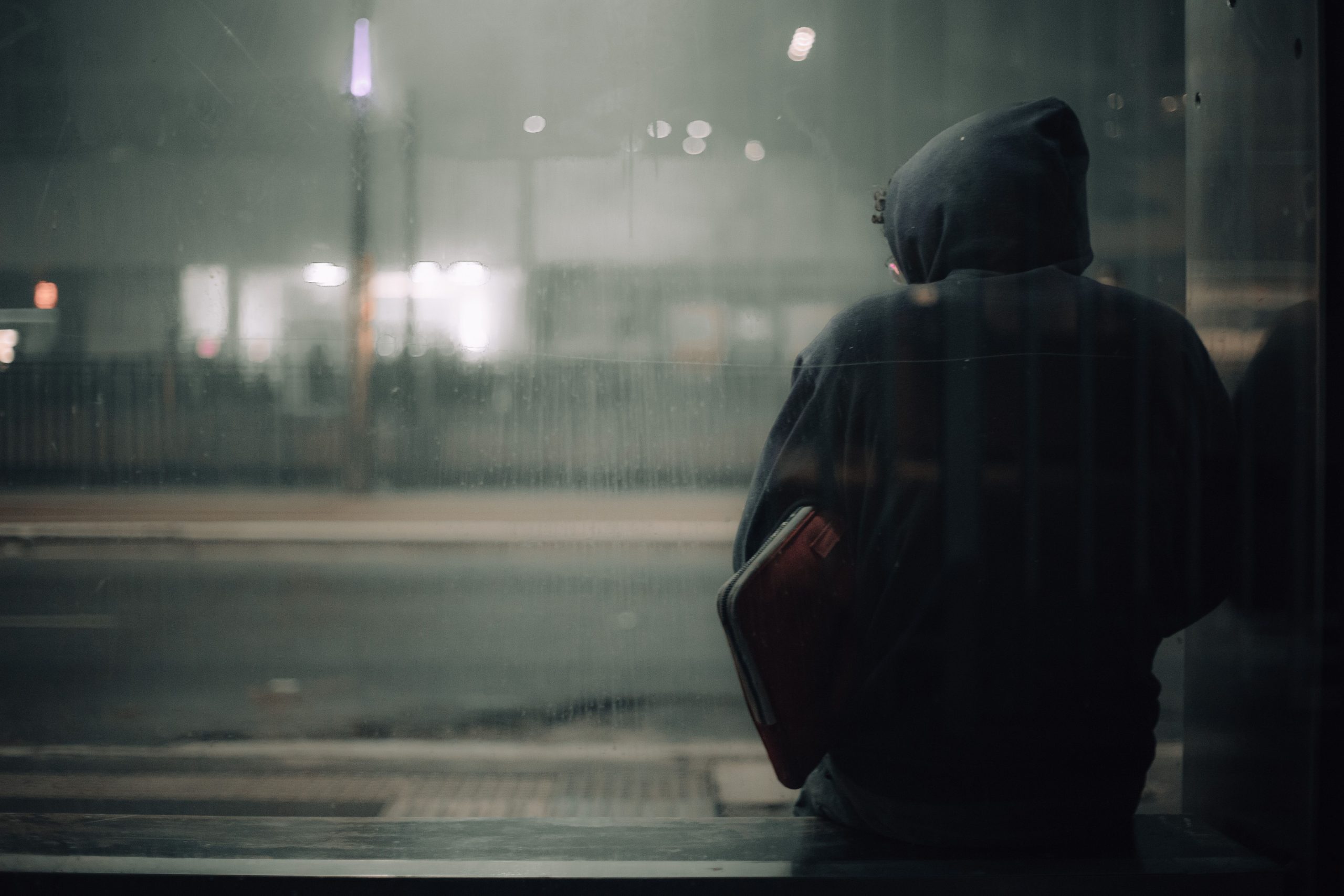 A person sits alone at night in an urban setting, reflecting the isolation that can drive people to seek connection.
